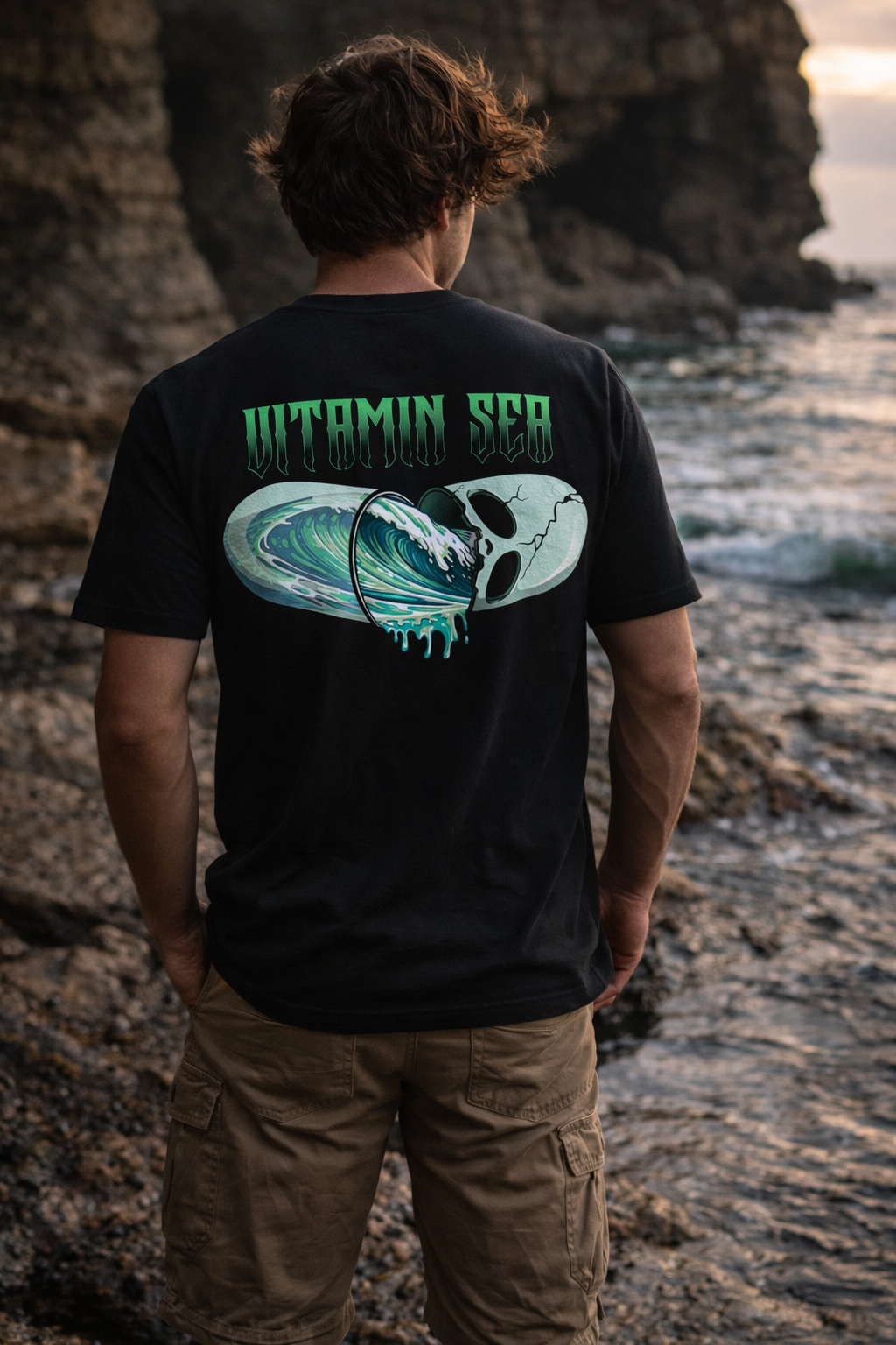 Person wearing a black t-shirt with 'Vitamin Sea' design by the ocean.